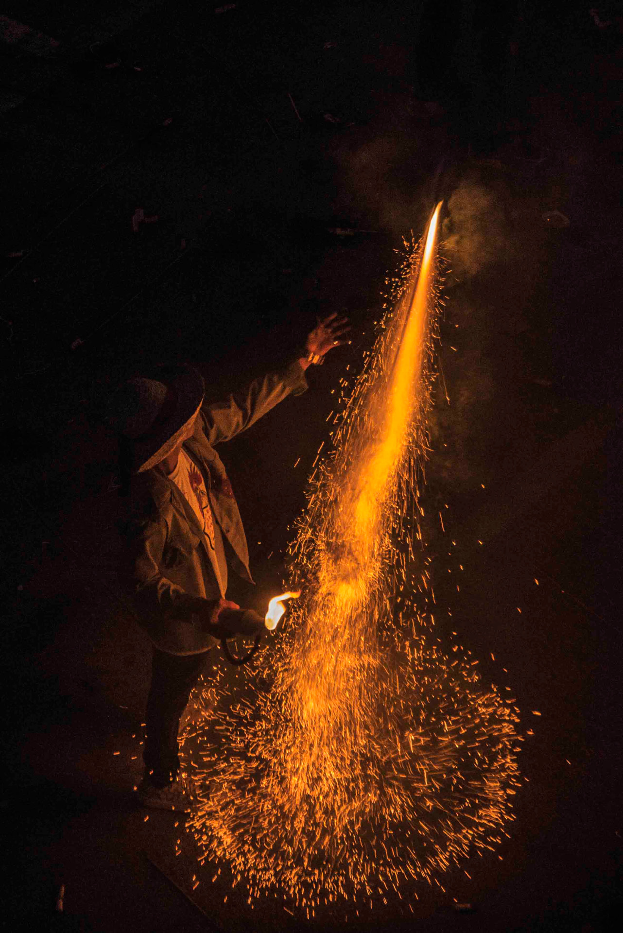 Un hombre enciende fuegos artificiales en la oscuridad, con una lluvia de chispas doradas